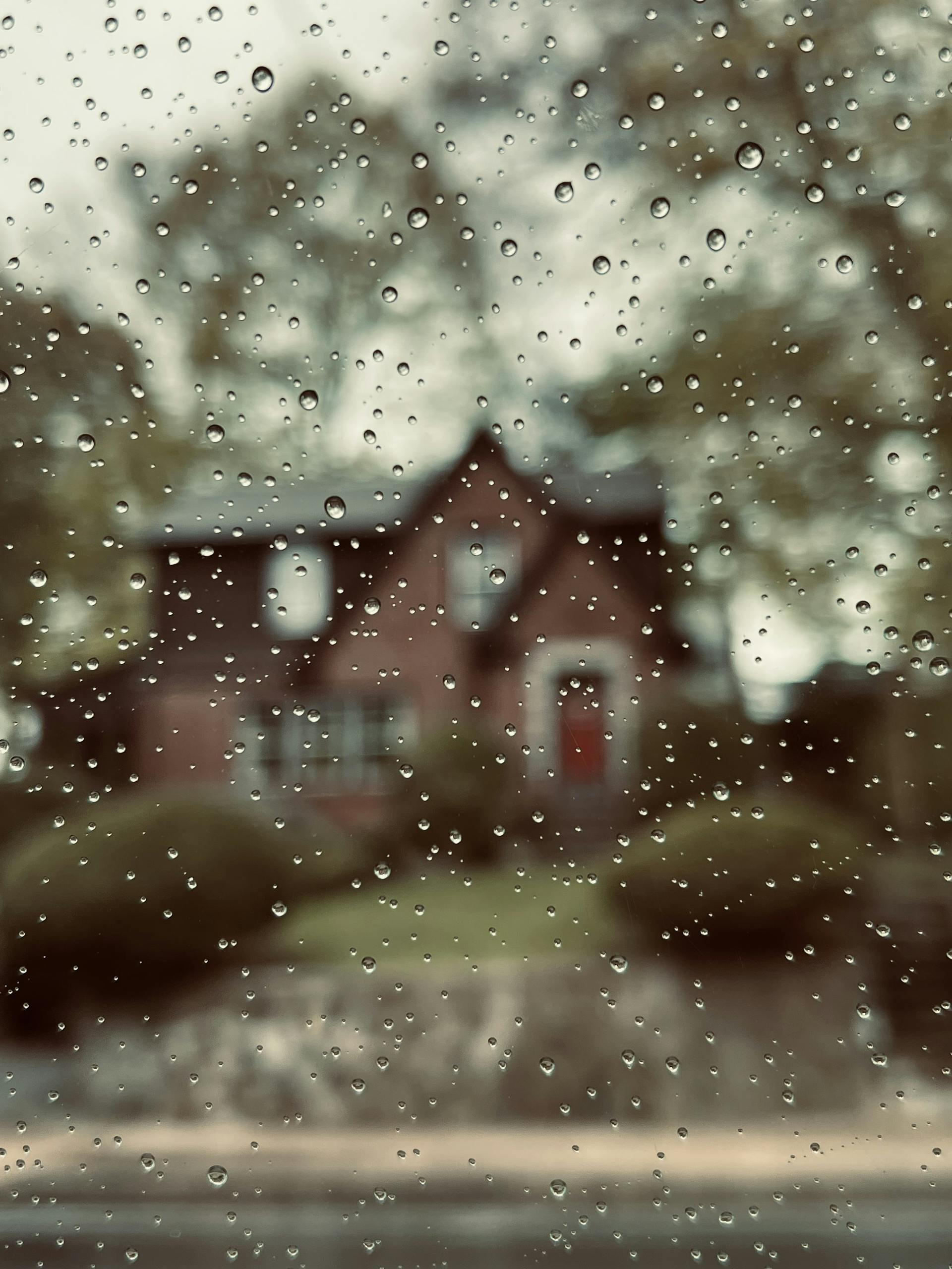 Artistic photo capturing raindrops on a window with a blurred house in the background.